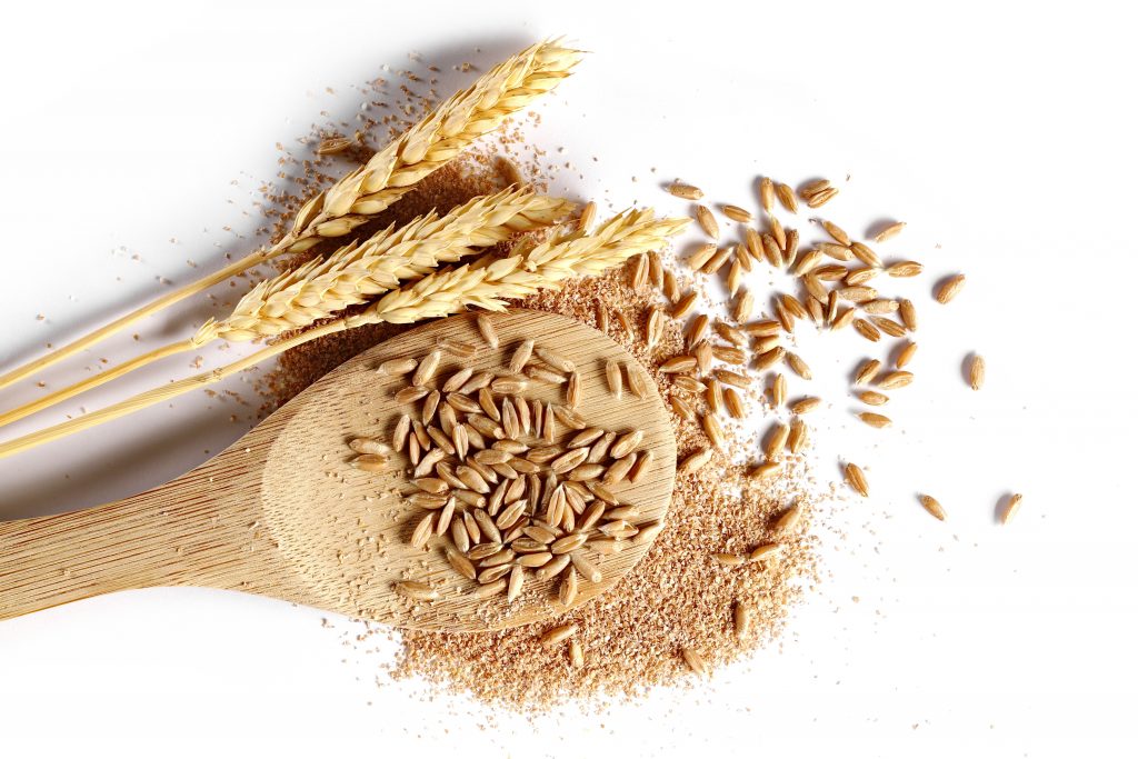 Spelt bran and grains with wooden spoon and ears of wheat isolated on white background, top view